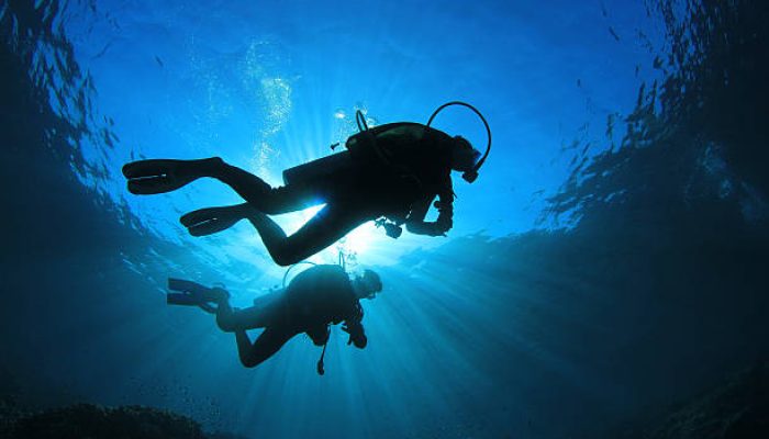 Two scuba divers silhouetted against the sun while they explore a coral reef